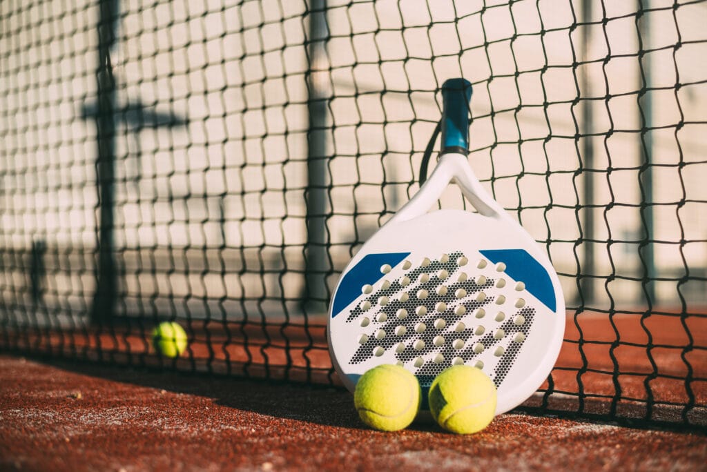 Raquette de padel contre un filet avec balles jaunes représentant les sports en P et les sports lettre p actuels