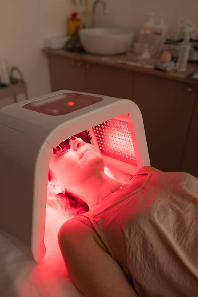 Personne allongée sous un appareil LED diffusant une lumière rouge, avec lunettes de protection, pendant une thérapie lumière rouge.